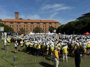 A large crowd of participants in yellow and white gear gathering for the Can4Cancer charity event on a sunny day.