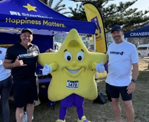 Two participants in Stryde4 event posing with a star mascot in front of a Starlight Children's Foundation tent